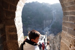 Kinesisk pojke balanserar överst på trappsteget med en orolig mamma som tittar på, Mutianyu Great Wall.