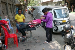 Utomhus-barberare i full färd med att raka en kund, Phnom Penh.