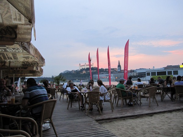 Party crowd vid konstgjorda beachen längs Donau med Bratislava castle i bakgrunden, Petrzalka, Bratislava.