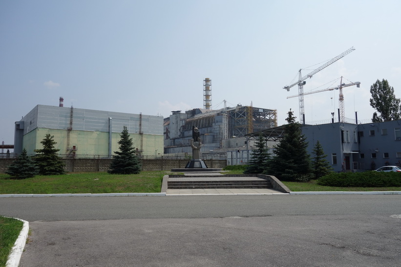 Monumentet för Tjernobyl-katastrofen i förgrunden och den havererade reaktor 4 i bakgrunden, Tjernobyl.